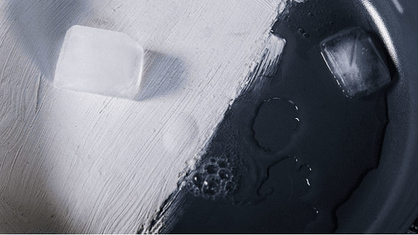 A close-up of a dark, textured surface split diagonally from white, with two translucent ice cubes resting on the surface.